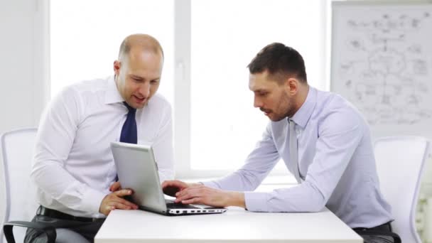 Два улыбающихся бизнесмена с ноутбуком в офисе — стоковое видео