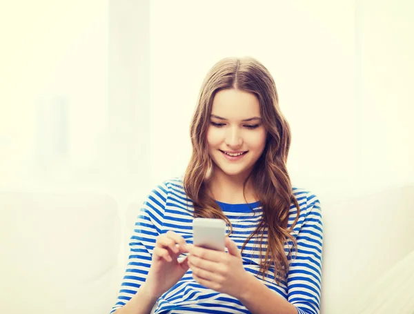 Улыбающаяся девочка-подросток со смартфоном дома — стоковое фото