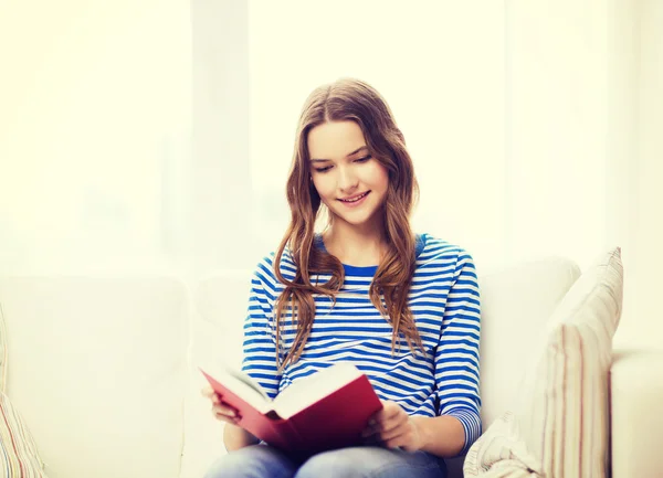 Uśmiechający się nastolatka czytanie książki na kanapie — Zdjęcie stockowe