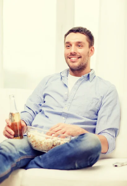 Glimlachende man met bier en popcorn thuis — Stockfoto