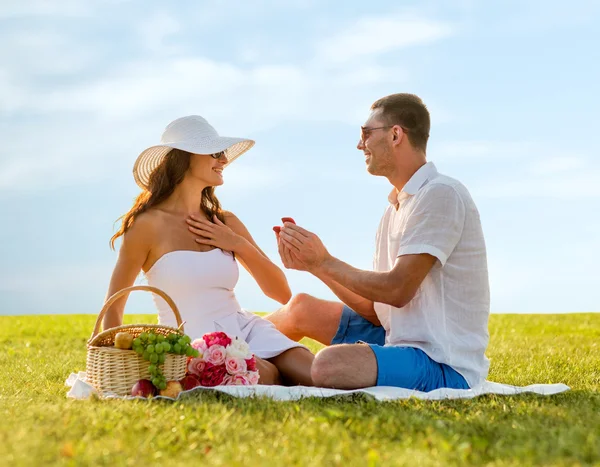 Sonriente pareja con pequeña caja de regalo roja en el picnic —  Fotos de Stock