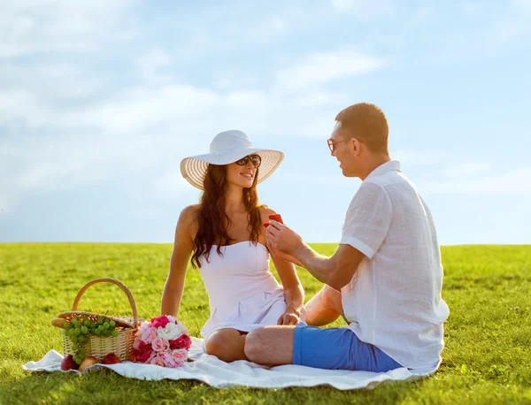 Sonriente pareja con pequeña caja de regalo roja en el picnic —  Fotos de Stock