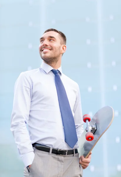 Joven hombre de negocios sonriente con monopatín al aire libre — Foto de Stock