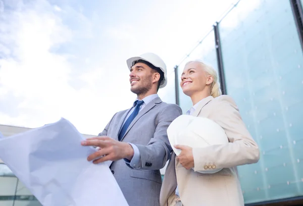 Glimlachende zakenmensen met blauwdruk en helmen — Stockfoto