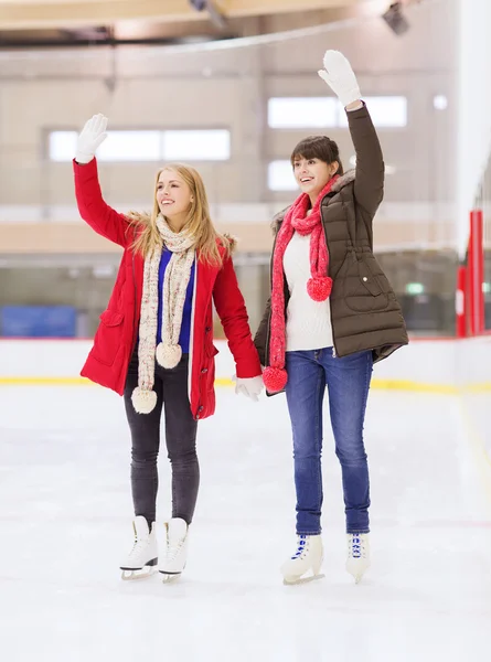 Chicas felices amigos agitando las manos en pista de patinaje — Foto de Stock