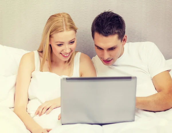 ノート パソコンと一緒にベッドでカップルの笑みを浮かべてください。 — ストック写真