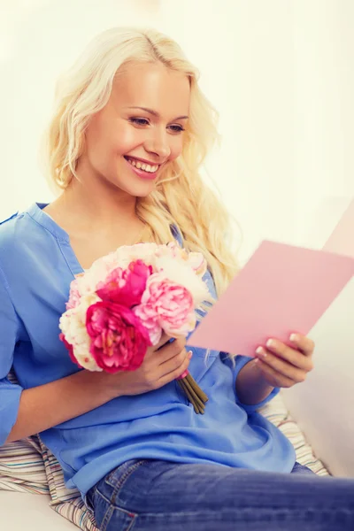 Mulher sorridente com cartão e buquê de flores — Fotografia de Stock