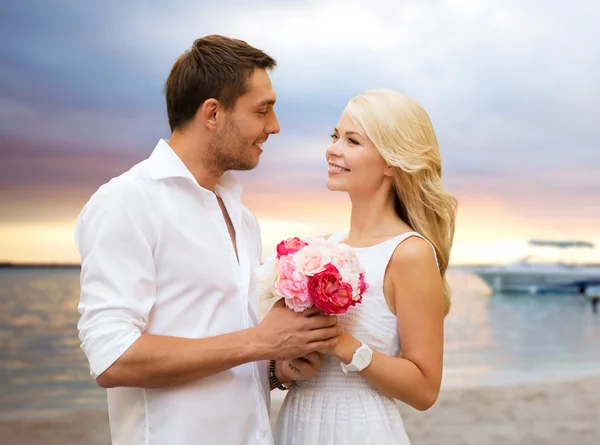 Gelukkige paar met bloemen over beach achtergrond — Stockfoto