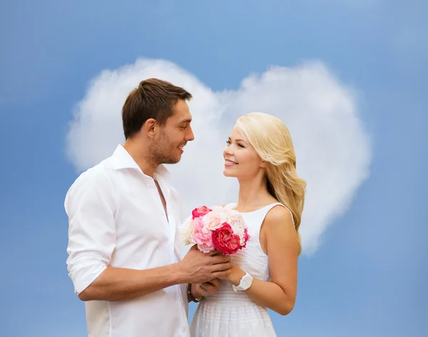 Happy couple with flowers over heart shaped cloud — Stock Photo, Image