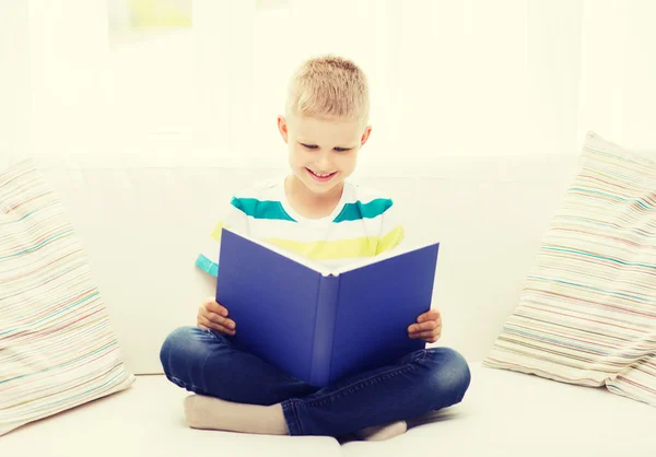 Sorrindo menino leitura livro no sofá — Fotografia de Stock