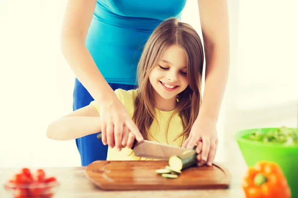 Sorrindo menina com a mãe cortando pepino — Fotografia de Stock