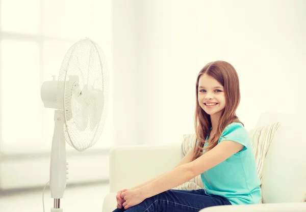 Petite fille souriante avec un grand ventilateur à la maison — Photo