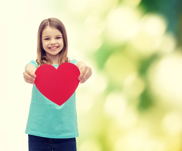 Kırmızı kalp veren küçük kız gülümseyerek — Stok fotoğraf