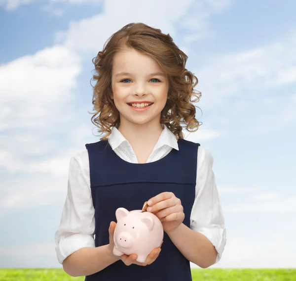 Lächelndes Mädchen steckt Münze in Sparschwein — Stockfoto