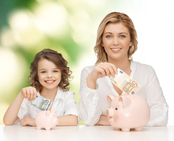 Mãe e filha colocando dinheiro para porquinhos bancos Fotografias De Stock Royalty-Free