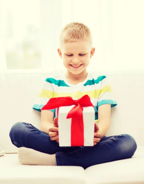 Smiling little holding gift box sitting on couch — Stock Photo, Image