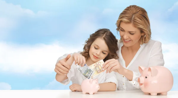 mother and daughter putting money to piggy banks