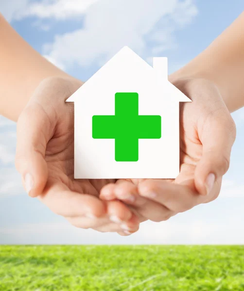 Händer som håller papper hus med grönt kors — Stockfoto