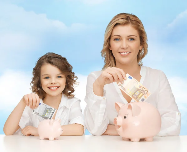 Mãe e filha colocando dinheiro para porquinhos bancos Fotografia De Stock