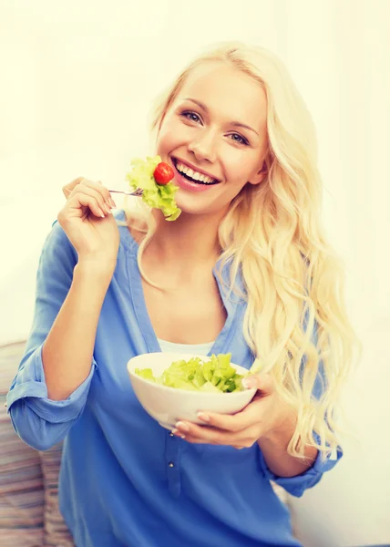 Lachende jonge vrouw met groene salade thuis — Stockfoto