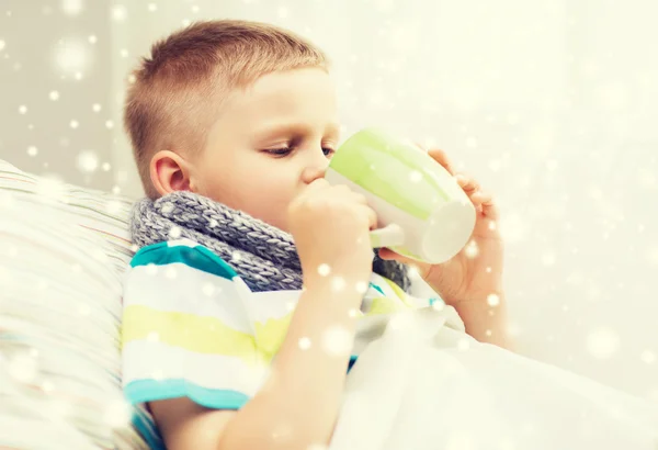 Ziek jongen met griep in bed drinken uit een beker thuis — Stockfoto