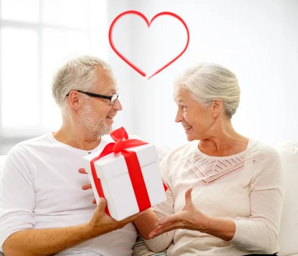 Feliz pareja de ancianos con caja de regalo en casa — Foto de Stock