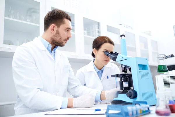 Cientistas com área de transferência e microscópio em laboratório — Fotografia de Stock