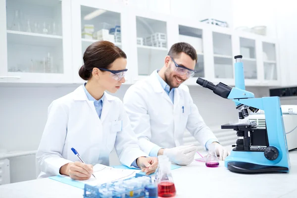 Científicos con portapapeles y microscopio en laboratorio —  Fotos de Stock