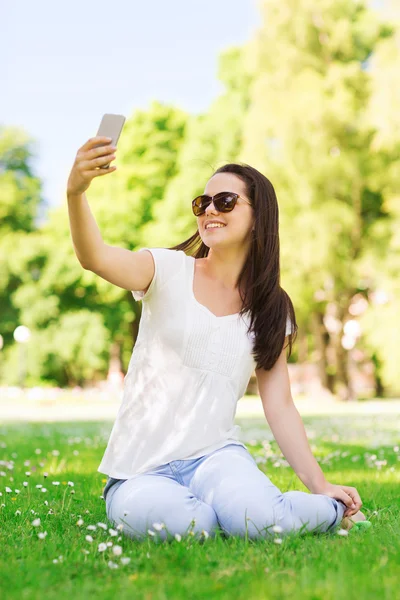 Niña sonriente con teléfono inteligente sentado en el parque — Foto de Stock