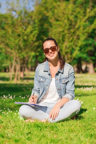 Smiling young girl with notebook writing in park — Stock Photo, Image
