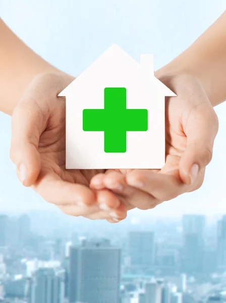 Hands holding paper house with green cross — Stock Photo, Image