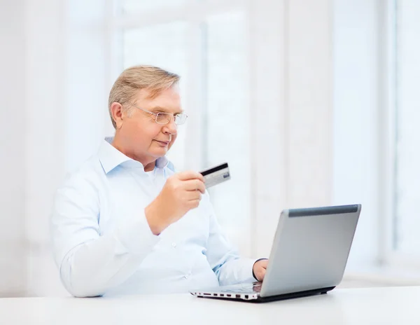 Oude man met laptop en een creditcard bij u thuis — Stockfoto