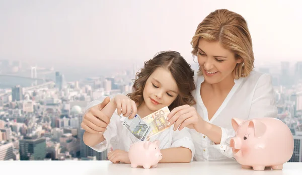 Matka a dcera, dát peníze na Prasátko Bank Royalty Free Stock Fotografie