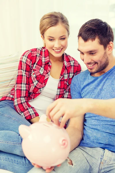 Smiling couple with piggybank sitting on sofa — Stock Photo, Image