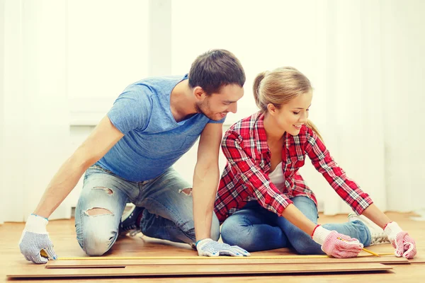 Coppia sorridente misurazione pavimenti in legno — Foto Stock