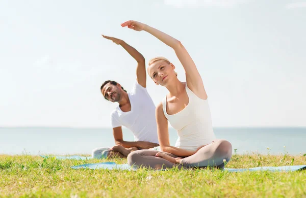 Sorrindo casal fazendo exercícios de ioga ao ar livre — Fotografia de Stock