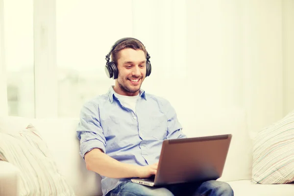 Sorrindo homem com laptop e fones de ouvido em casa — Fotografia de Stock
