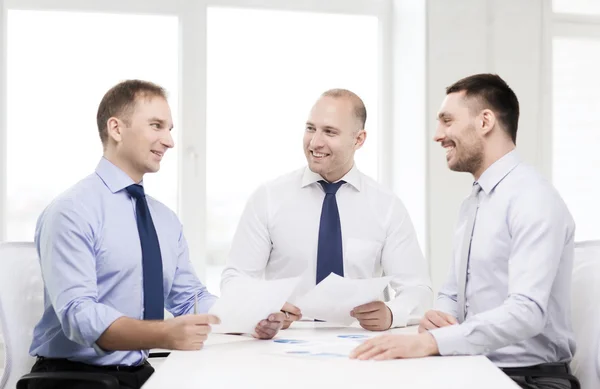 Hombres de negocios sonrientes con papeles en la oficina — Foto de Stock