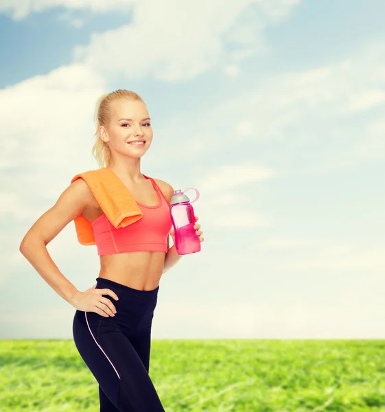 Lächelnde sportliche Frau mit Wasserflasche und Handtuch — Stockfoto