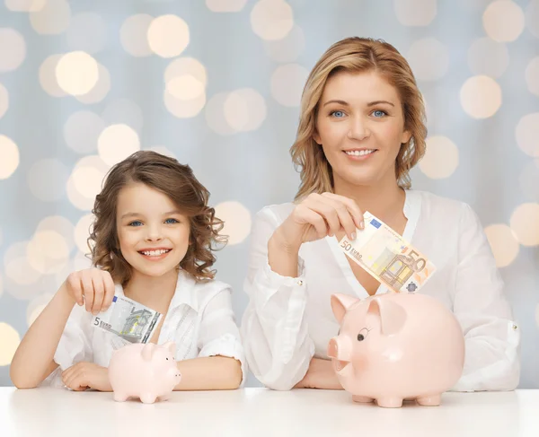 Mutter und Tochter legen Geld in Sparschweine — Stockfoto