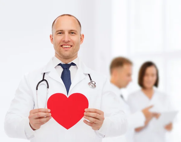 Sorridente médico masculino com coração vermelho e estetoscópio — Fotografia de Stock