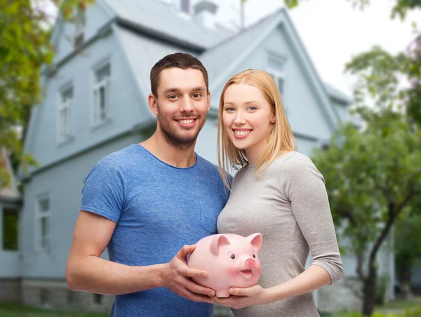 Smiling couple holding piggy bank over house — Stock Photo, Image