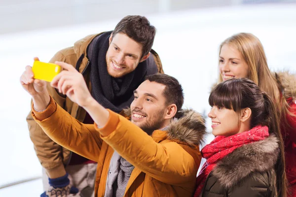 Happy friends with smartphone on skating rink Royalty Free Stock Photos