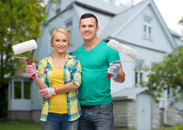 Lachende paar met verf rollen over huis — Stockfoto