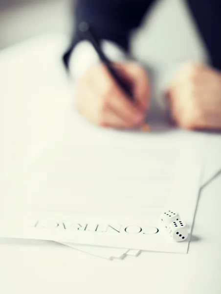 Man hands with gambling dices signing contract — Stock Photo, Image