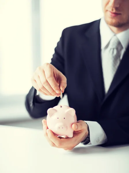 Hombre poniendo moneda en una pequeña alcancía —  Fotos de Stock