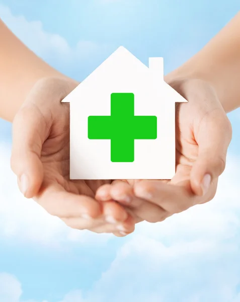 Hands holding paper house with green cross — Stock Photo, Image