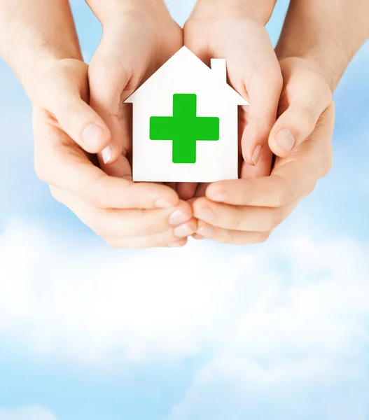 両手緑の十字と紙の家 — ストック写真