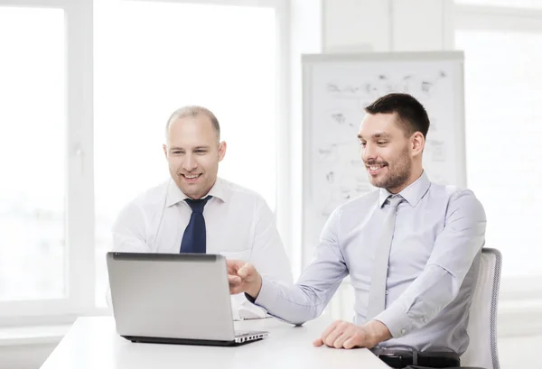 Two smiling businessmen with laptop in office — Stock Photo, Image