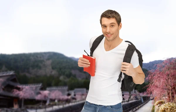 Felice giovane uomo con zaino e prenotare in viaggio — Foto Stock